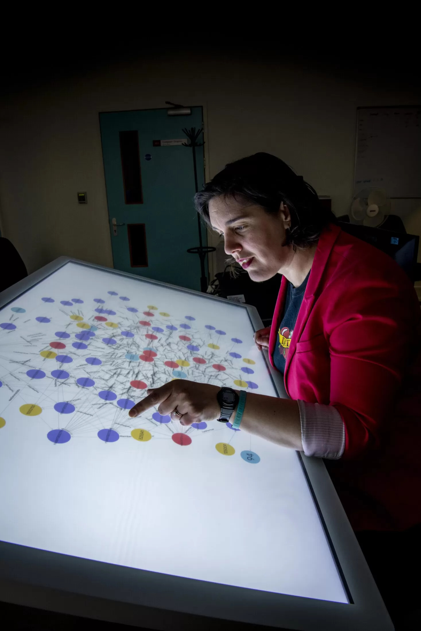A member of staff wearing a pink blazer examines a large backlit screen