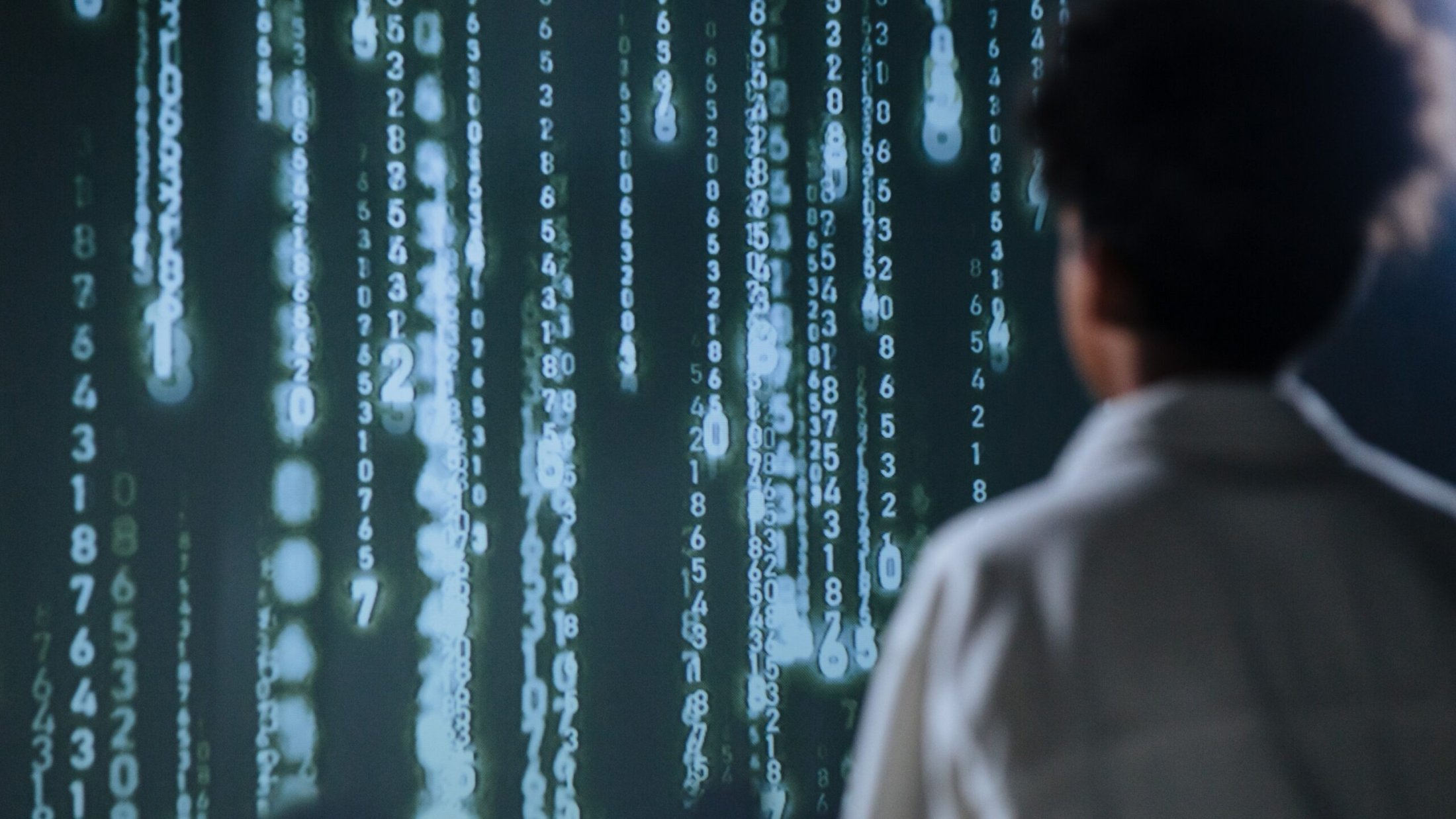 Person observing cascading numbers on a screen resembling digital rain.