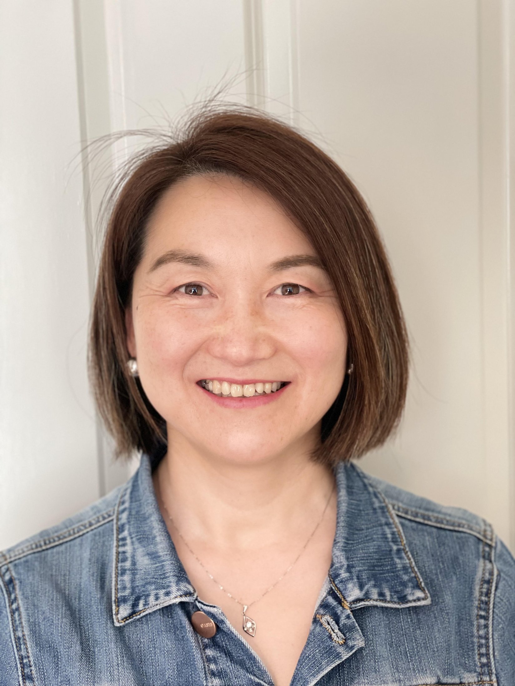 A smiling woman, Dr Haiming Liu, with short brown hair, wearing a blue washed denim casual shirt.