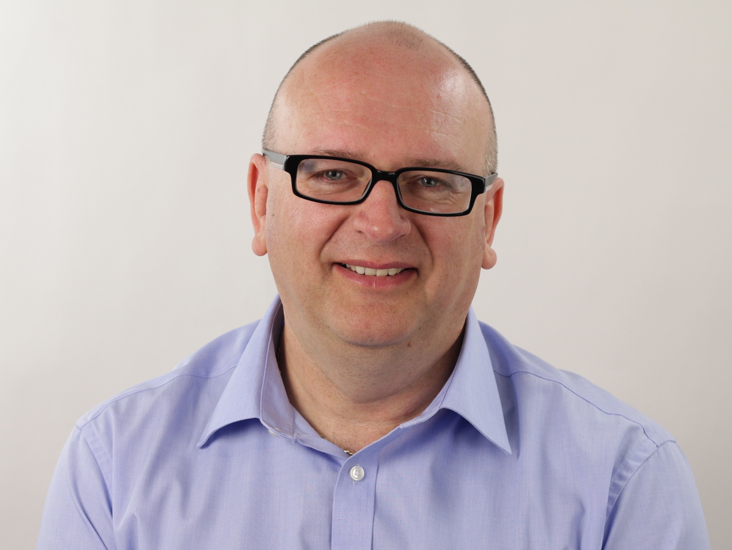 A smiling man, Professor Neil White, with very short dark hair and wearing black rectangular plastic glasses. He is wearing a purple shirt.