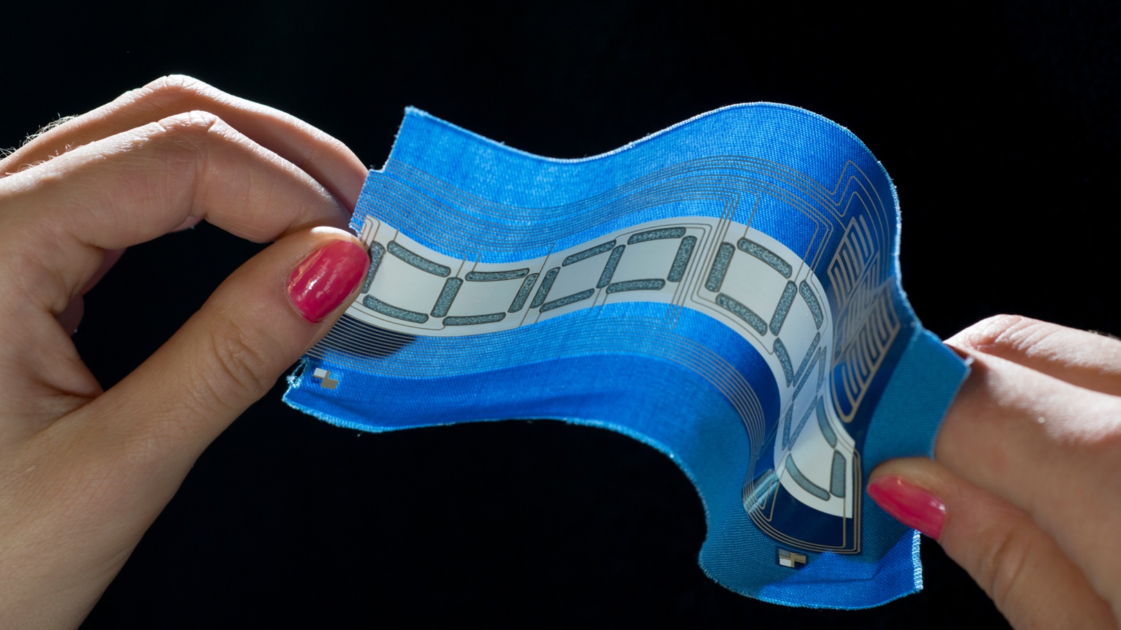 Close-up of a pair of hands holding a flexible, blue fabric embedded with silver circuitry.